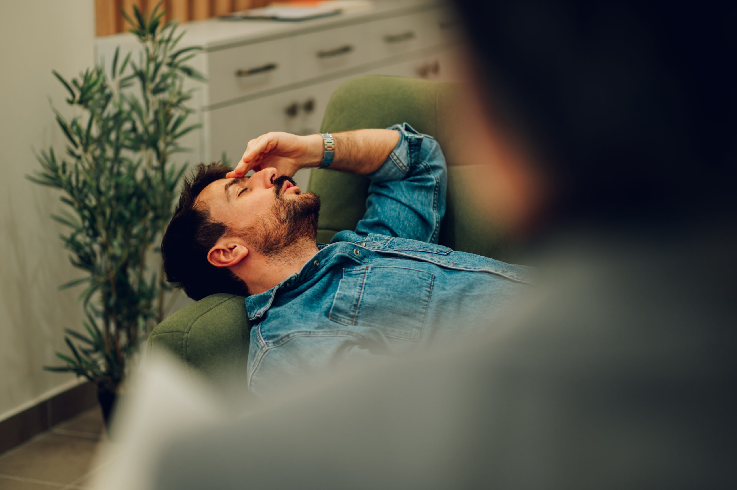 A sad patient with a mental disorder is lying down on a sofa in a psychotherapist's office and discussing his feelings and trauma. An anxious client talks on the therapist's couch during his session.